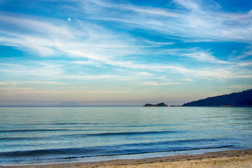 Obraz premium Tranquil ocean scene with moon rising, islands, coastline, and wispy clouds during twilight