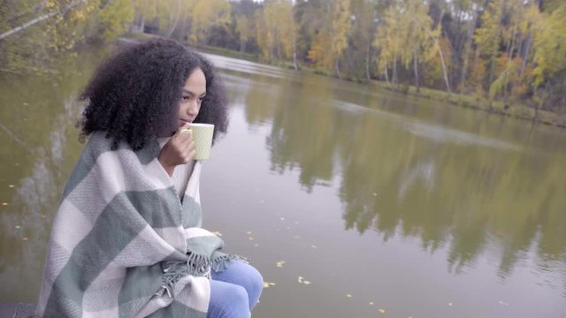 Cute black girl wrapping herself in woolen plaid and drinking hot tea