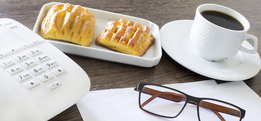 Office workplace. Croissants with coffee and telephone on the wooden table