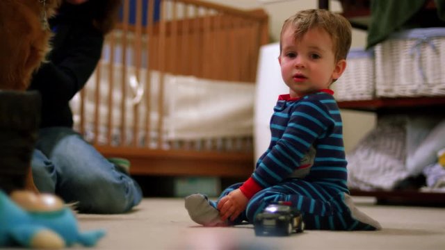 Adorable little boy in pajamas plays with a toy police car on the floor in his room