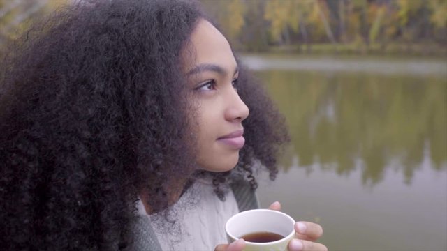 Cute black girl wrapping herself in woolen plaid and drinking hot tea