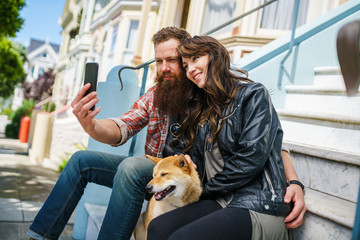 couple sitting on steps of painted ladies in san francisco with pet dog