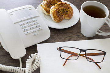 Office workplace. Croissants with coffee and telephone on the wooden table