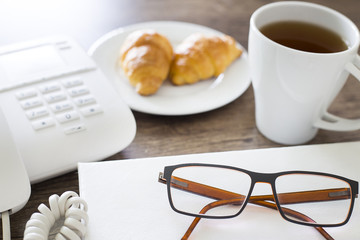 Office workplace. Croissants with coffee and telephone on the wooden table