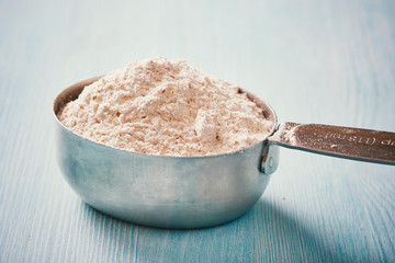 Measuring cup spoon with flour on blue wooden table