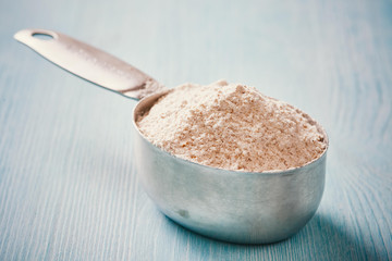 Measuring cup spoon with flour on blue wooden table