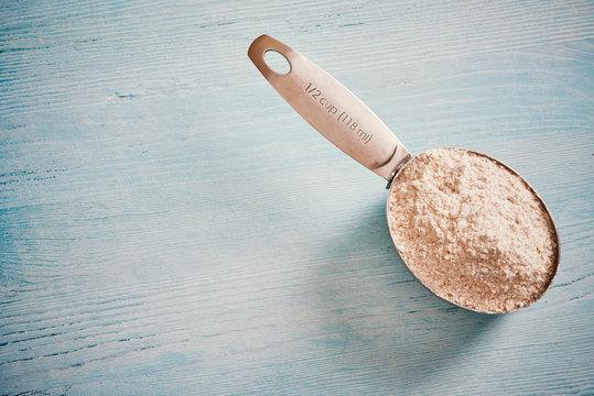 Measuring cup spoon with flour on blue wooden table - text space on the left