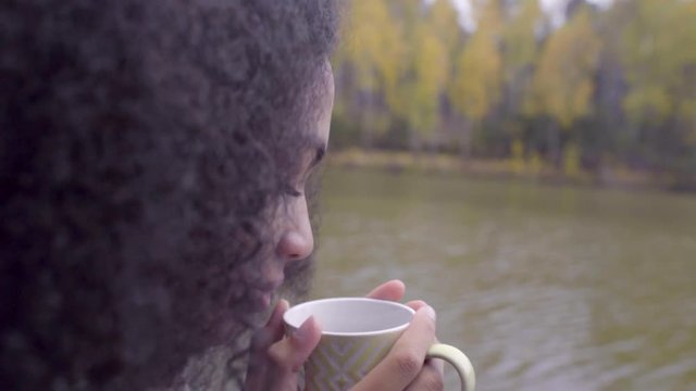 Cute black girl wrapping herself in woolen plaid and drinking hot tea