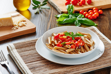 Pasta with cherry tomatoes and basil on white dish surrounded by ingredients