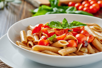 Pasta with cherry tomatoes and basil on white dish, ingredients in background
