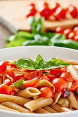 Pasta with cherry tomatoes and basil on white dish, ingredients in background