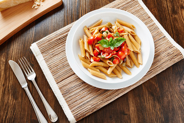 Pasta with cherry tomatoes and basil on white dish on wooden table
