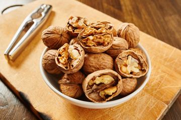 Walnuts in bowl and nutcracker on a cutting board and wooden table
