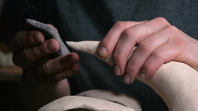 Artist is polishing a piece of clay horn abstract object before glazing in the ceramic workshop