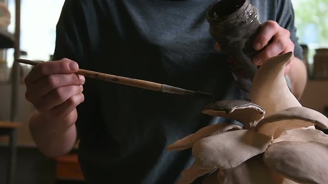 Artist is glazing dried clay abstract object before the glaze firing