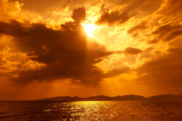 Fototapeta premium Złocisty rozbłysk słońca między chmurami na morskim horyzocie