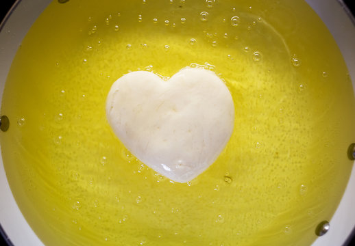 A heart shaped donut deef frying in a pan of bubbling oil