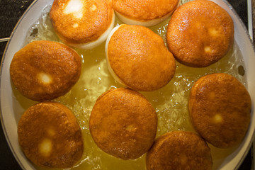 A frying pan with hot bubbling oil full of browned donuts without the holes