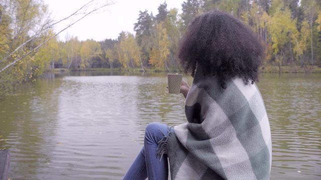 Cute black girl wrapping herself in woolen plaid and drinking hot tea