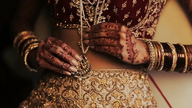 Indian bride's long finders hold a golden pendant hanging over her red costume