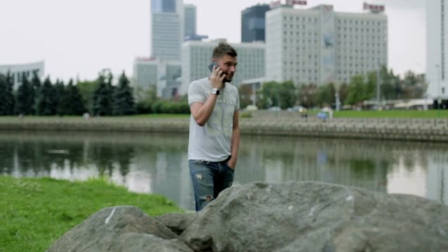 Attractive young man standing near a big stone and talking on mobile phone.