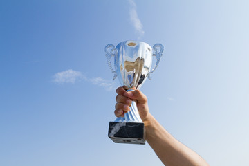 Athlete holding up champion winner trophy cup on sky background