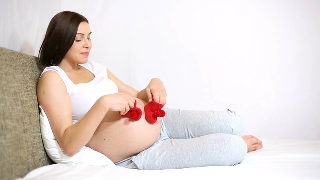 Pregnant woman holding little shoes in the living room