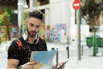 A young man with a map and smartphone gps in the city