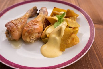 Roasted chicken drumsticks served on the old vintage porcelain plate with baked sweet potatoes and...