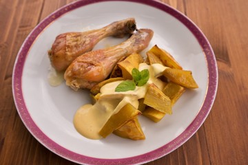 Roasted chicken drumsticks served on the old vintage porcelain plate with baked sweet potatoes and french mustard sauce. Picture isolated on the wooden table closeup. Fresh and healt family lunch.