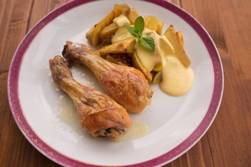 Roasted chicken drumsticks served on the old vintage porcelain plate with baked sweet potatoes and french mustard sauce. Picture isolated on the wooden table closeup. Fresh and healt family lunch.