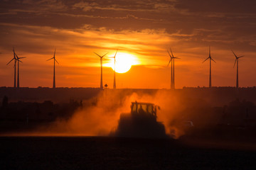 Fototapeta premium Bauer bei der Ernte im Sonnenuntergang vor Windrädern