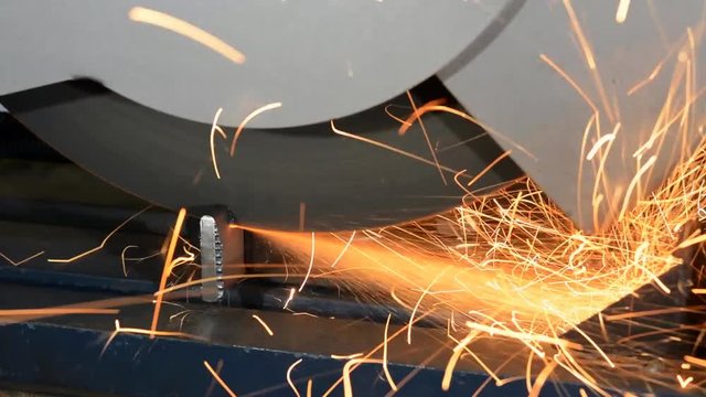 A radial arm saw cuts through some square steel stock, throwing out hot sparks