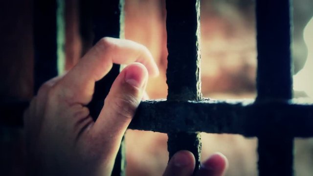 Man angrily grabs prison bars as if he were upset.