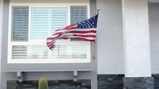 American flag blowing in the breeze while hanging on a residential home symbolizes a patriotic holiday in the United States..