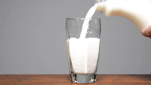Cold, fresh milk being poured into a drinking glass against a gray background. Room for copy to the left of the glass. .