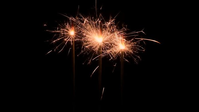 Three burning gold firework sparklers emitting sparks against a black background.