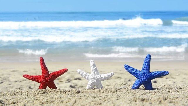 Conceptual summer holiday video of three red, white and blue starfish on the beach overlooking a turquoise ocean while celebrating the July fourth holiday. .
