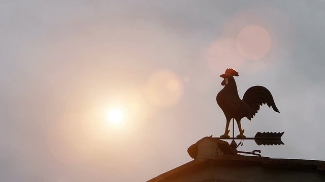 Weather vane in rooster shape on the roof, sun raising.Time lapse, lens flare