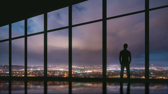 5 in 1 video! The man stand at the panoramic window on the background of night the city. Time lapse. Wide angle