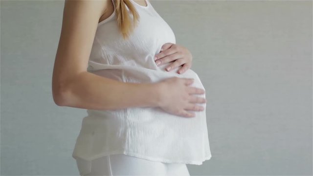 Girl in a white blouse carefully stroking her belly, and preparing to become a mother.