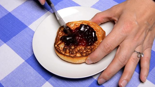 A woman at a diner spreads grape jelly on her freshly toasted English muffin before eating it.