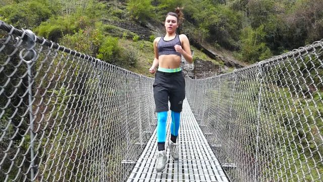 Young woman in the sports clothing running across the suspension bridge in the Himalayan mountains.Slow motion, high speed camera