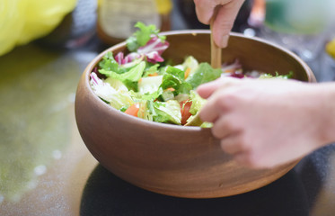 Healthy green salad being tossed in wooden bowl on counter