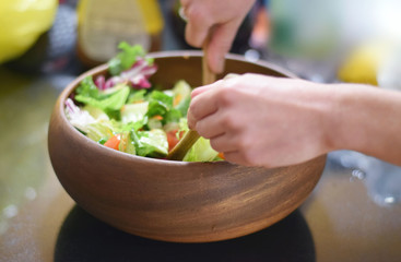 Healthy green salad being tossed in wooden bowl on counter
