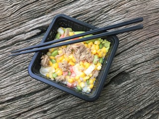 Tuna corn salad on black bowl and chopstick on wood background