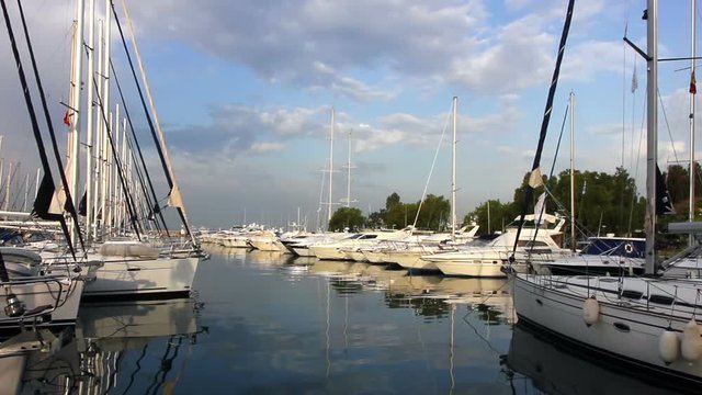 Row of white luxury yachts in harbor, reflections in calm water, blue morning sky.