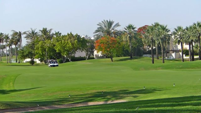 Perfect golf resort in Dubai city, with green grass, unrecognizable person in a background driving a golf vehicle