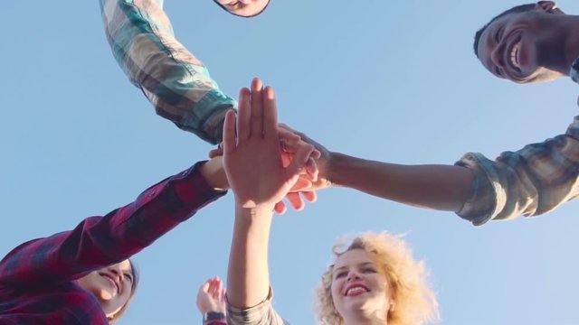 Slowmotion from below view of four friends putting their hands one on another, smiling and embracing .