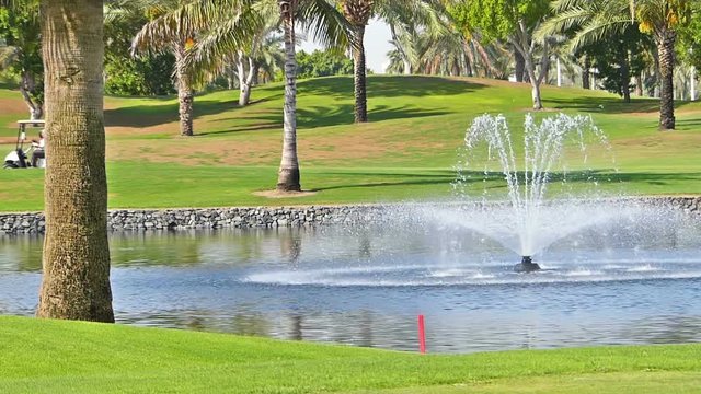 Perfect golf resort in Dubai city, with a fountain in a front, unrecognizable person in a background driving a golf vehicle